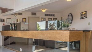 A reception area with a wooden reception desk, a clock, framed certificates, and a potted plant. - Rodeway Inn Fallsview (Niagara Falls)