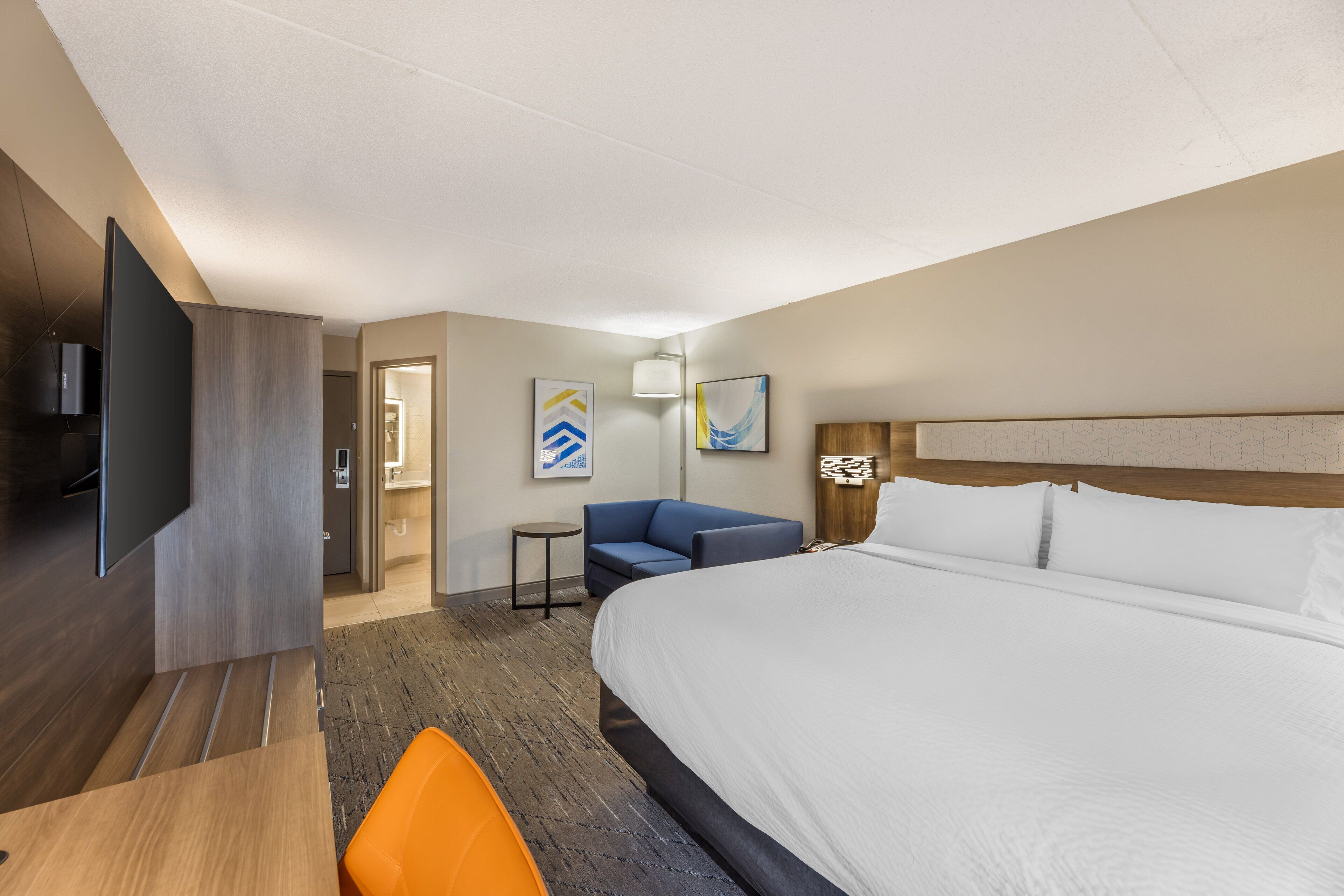 Ein Hotelzimmer mit einem großen Bett, einem Schreibtisch, einem Sessel, einem Fernseher und Bildern an den Wänden.