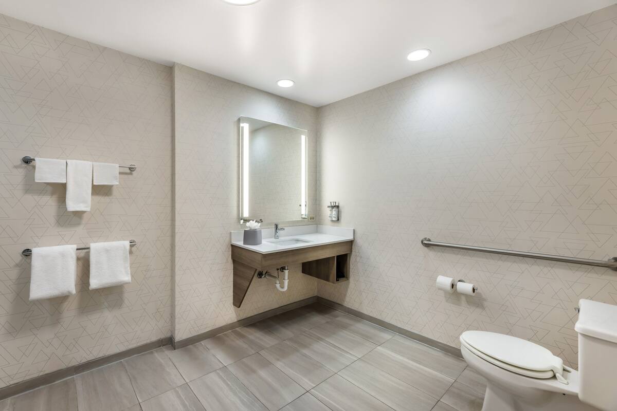 A modern bathroom with a sink, mirror, toilet, and handrails.