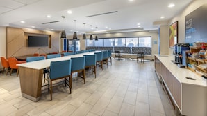A modern dining area with a long table, blue chairs, and a coffee station.