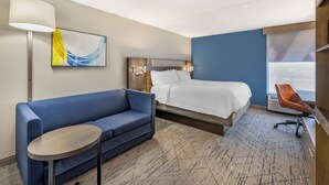 A hotel room with a bed, a blue sofa, a small table, a wall-mounted lamp, and a painting.