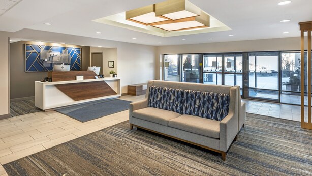 A modern lobby with a reception desk, a sofa, and large windows offering a view of the outside.