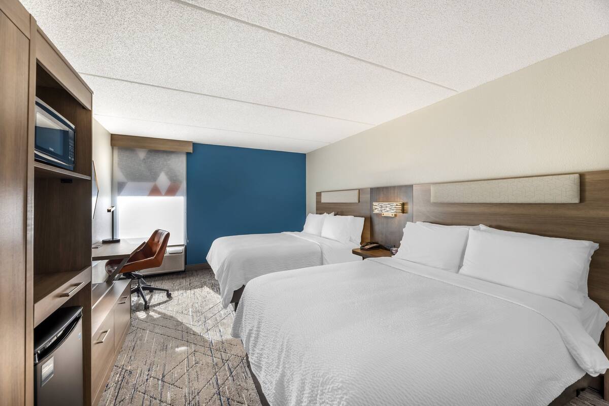 A hotel room with two beds, a desk, a chair, and a microwave.