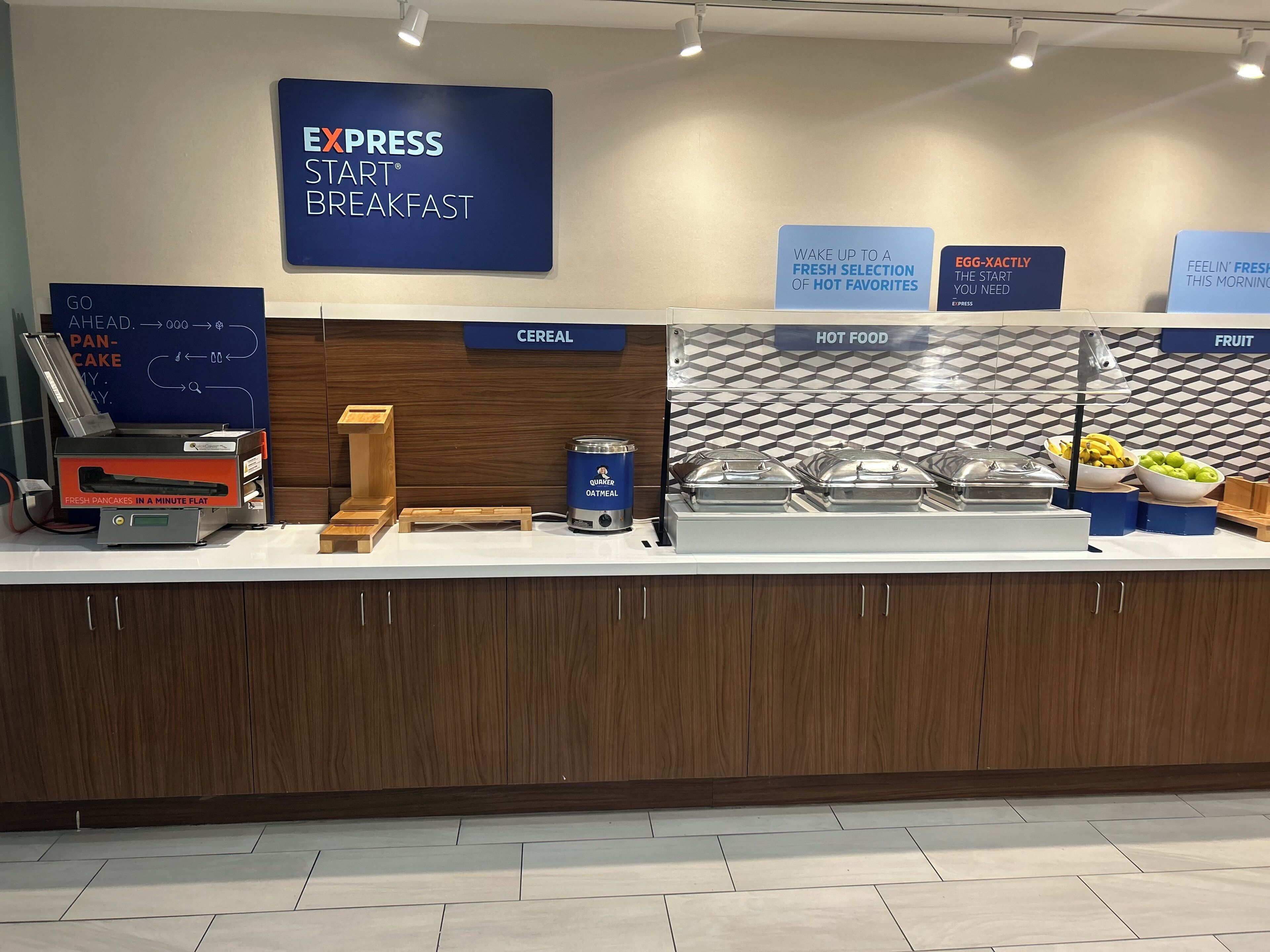 A breakfast buffet area with labeled sections for cereal, hot food, and fruit.