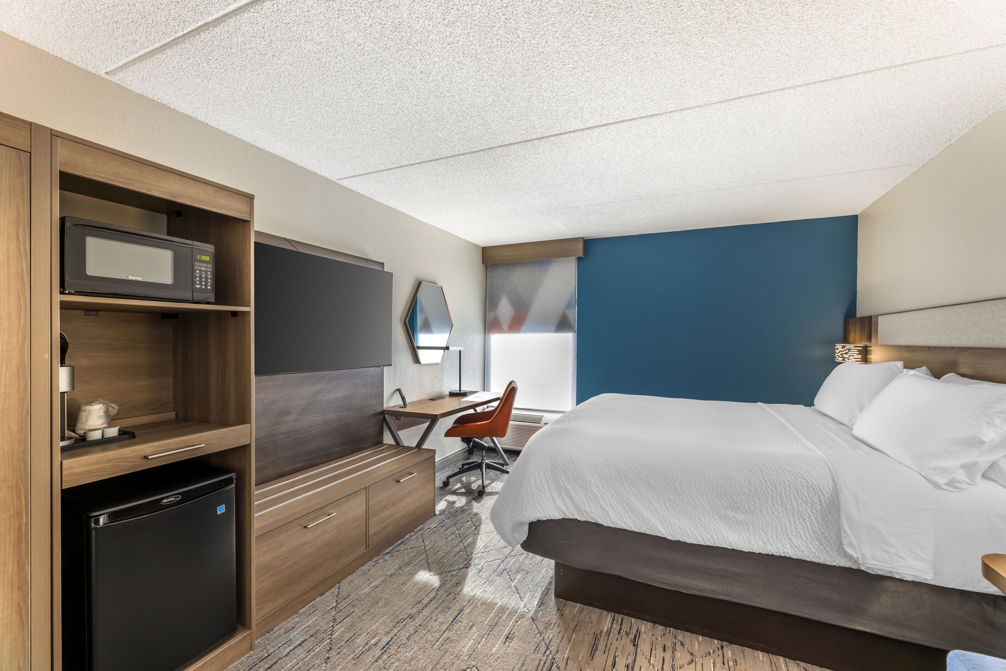 Een hotelkamer met een bed, een bureau met stoel, een magnetron en een minibar.