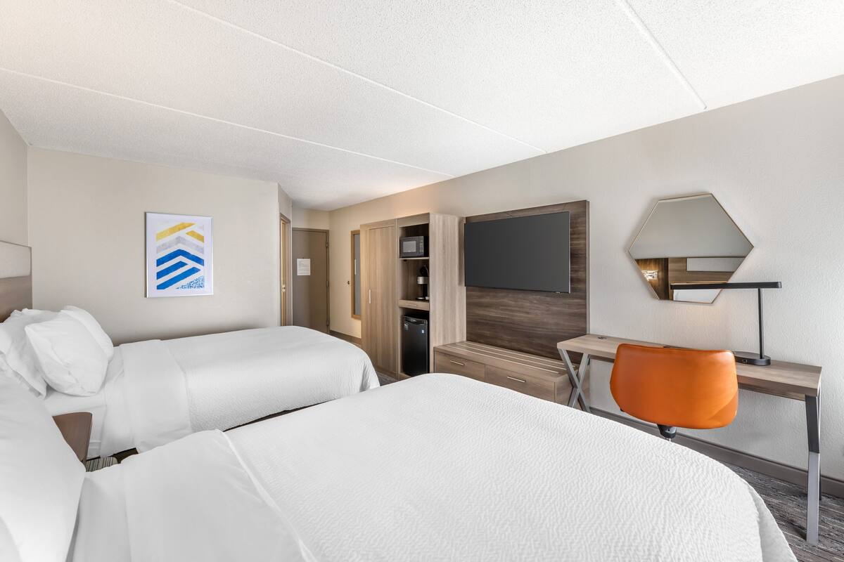 A hotel room with two beds, a desk, a chair, a flat-screen TV, and a microwave.
