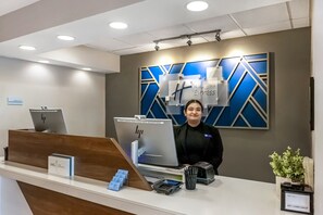 A hotel reception desk with a computer, a sign indicating no cash or credit card acceptance, and a plant on the right.