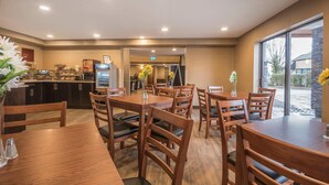 A restaurant with wooden tables and chairs, a counter with a coffee machine, and a view of the outside through large windows. - Comfort Inn (Chilliwack)