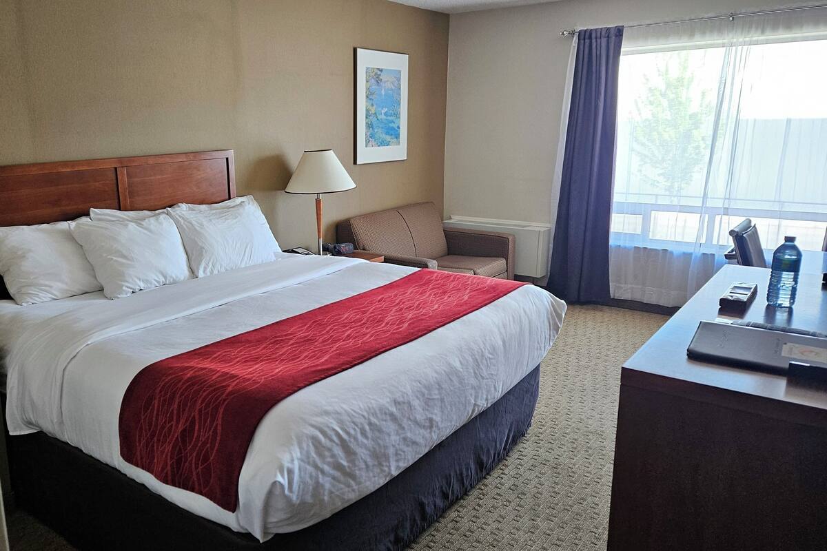 A hotel room with a large bed, a desk, a chair, a lamp, and a window with curtains.