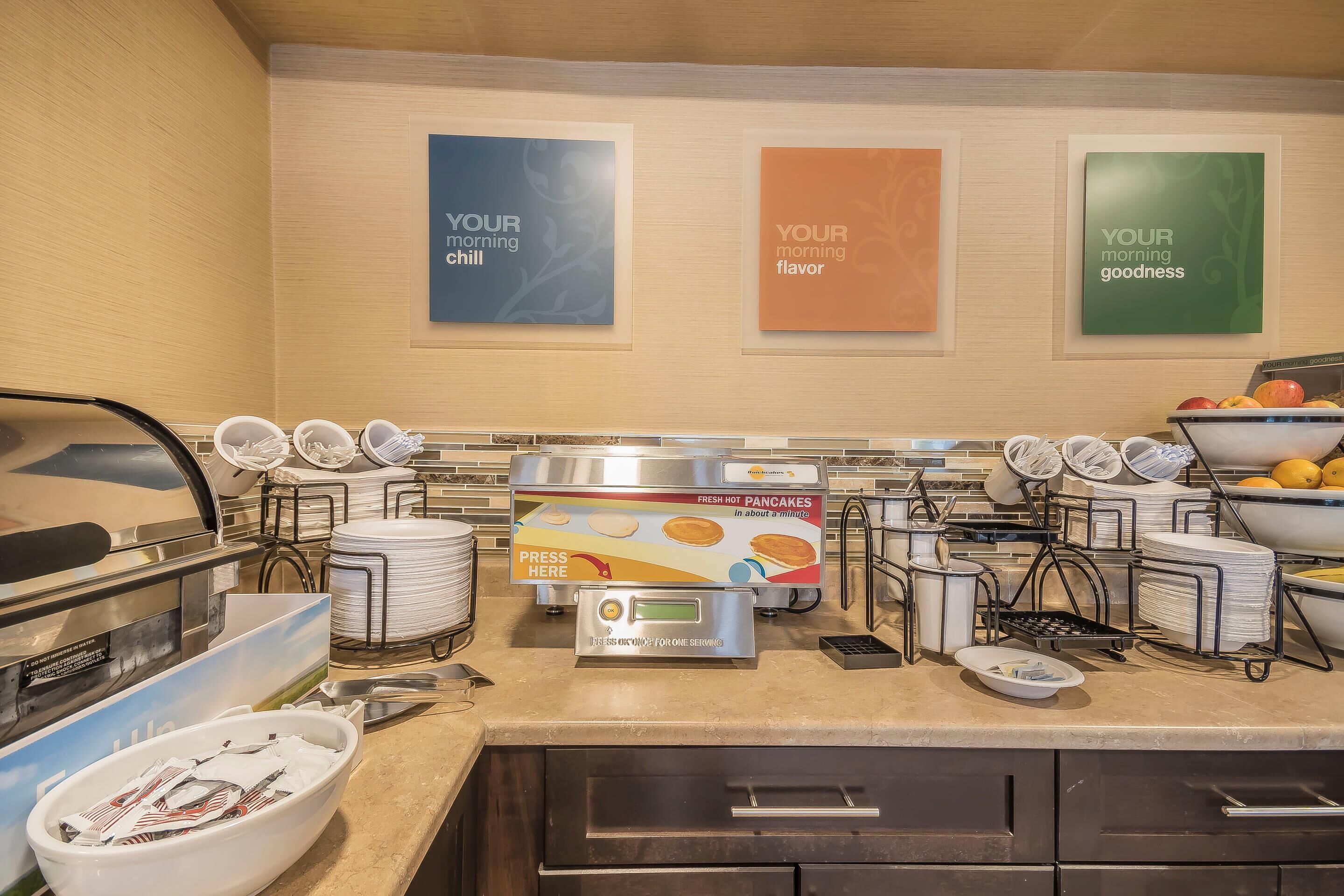 Zona de desayuno tipo buffet con estación de panqueques de servicio propio, tazones y platos.
