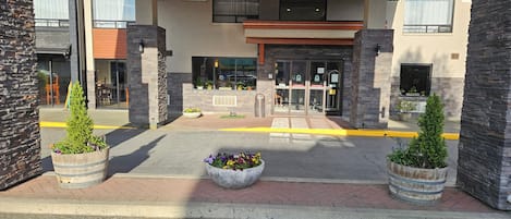 Una entrada moderna con pilares de piedra, un macizo floral central y un camino despejado hacia el acceso.