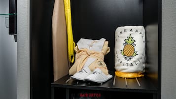 Un sèche-cheveux et une serviette à motifs d’ananas sont posés sur une étagère noire, dans une chambre d’hôtel.