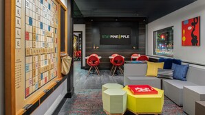 A modern lounge area with a Scrabble board, a large screen displaying "STAY PINEAPPLE", and a seating area with colorful chairs and sofas. - Staypineapple, Hotel FIVE, Downtown Seattle (Seattle)
