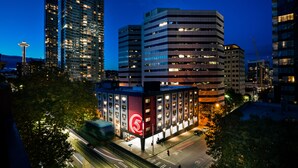 A cityscape at dusk with modern high-rise buildings, a prominent red logo on a building, and a view of the Space Needle. - Staypineapple, Hotel FIVE, Downtown Seattle (Seattle)