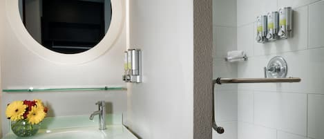 A bathroom with a glass sink, a round mirror, a shower with a glass door, and a towel rack.