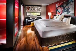 A modern hotel room with a large bed, a sofa, a small table, and a window with a view.