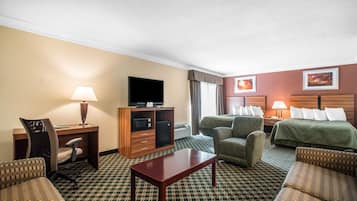 A hotel room with a bed, two armchairs, a desk with a lamp, a television, and a minibar.