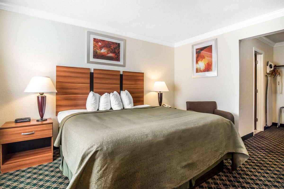 A hotel room with a bed, two bedside lamps, a wooden headboard, a nightstand, and two framed pictures on the wall.