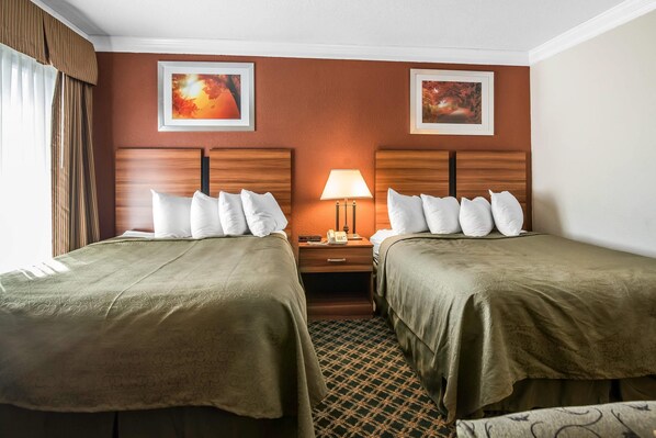 Une chambre d’hôtel avec deux lits, une table de chevet, une lampe et deux tableaux encadrés au mur.