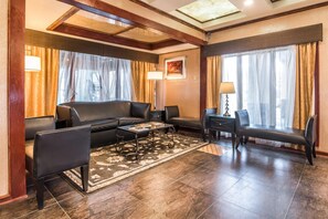 Een moderne woonkamer met een bank, fauteuils, een salontafel en een bureau. Er hangen gordijnen voor de ramen, een schilderij aan de muur en een kamerkleed op de vloer.