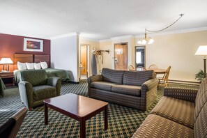 A hotel room with a green patterned sofa, a wooden coffee table, a patterned armchair, and a dining area with a wooden table and chairs. - Quality Inn Rutland - Killington (Rutland)