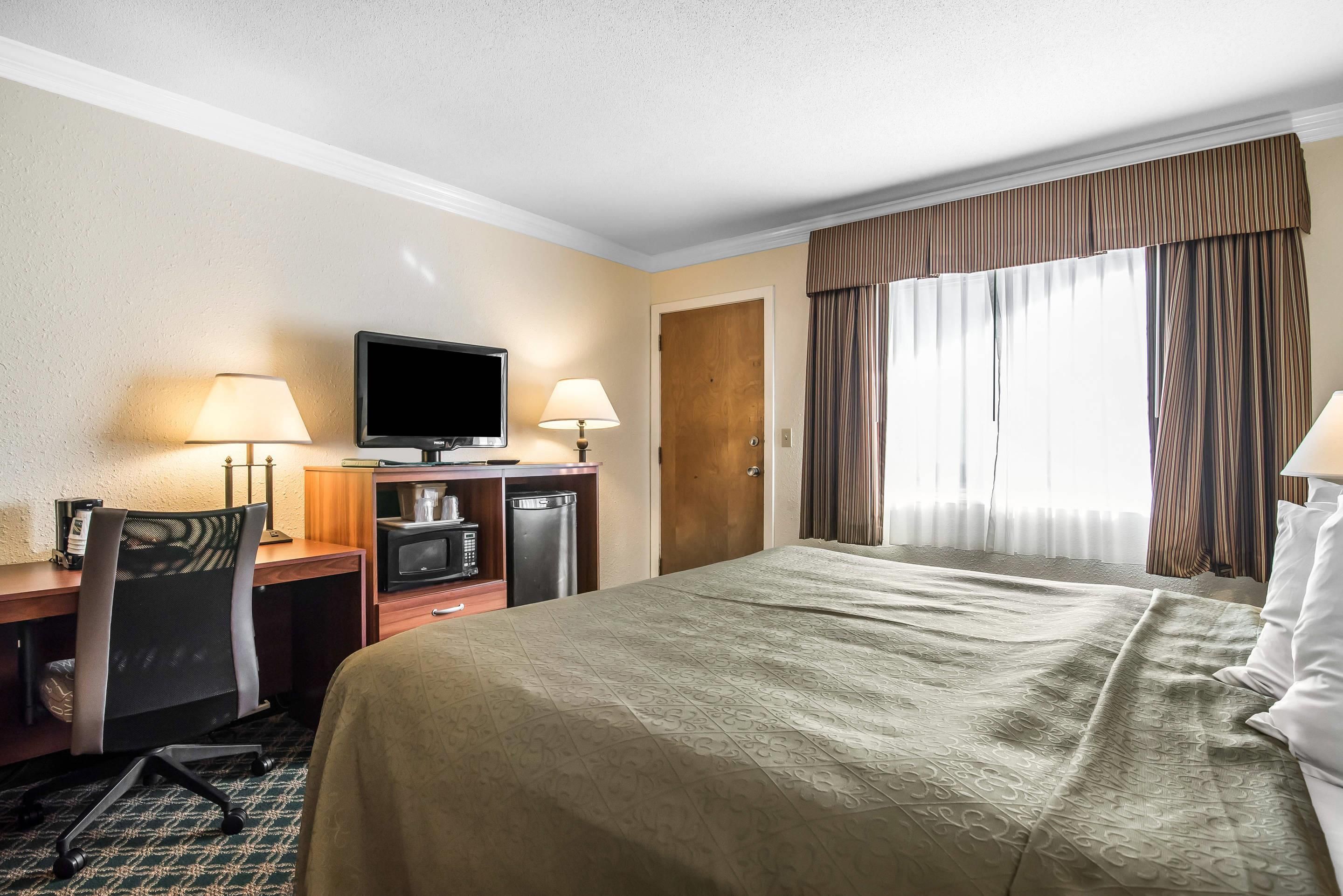 A hotel room with a bed, desk, television, and a window with curtains.