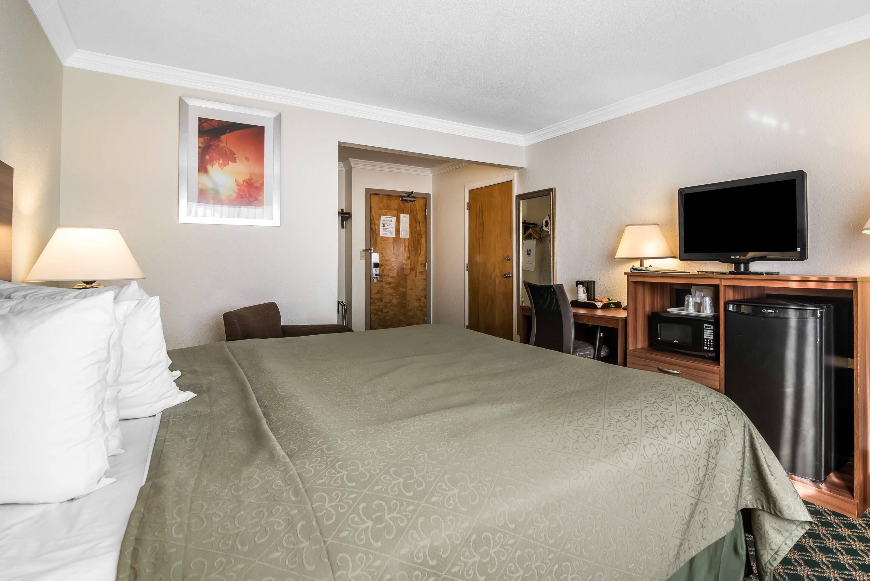 A hotel room with a bed, a desk, a television, and a refrigerator.