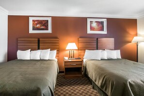 A hotel room with two beds, a nightstand, a lamp, and two framed pictures on the wall. - Quality Inn Rutland - Killington (Rutland)