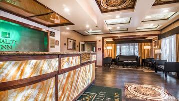 A hotel reception area with a marble counter, a green-lit sign, and a reception desk.