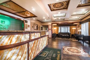 Een hotel receptie met een marmeren balie, een verlicht bord en een receptiebalie.