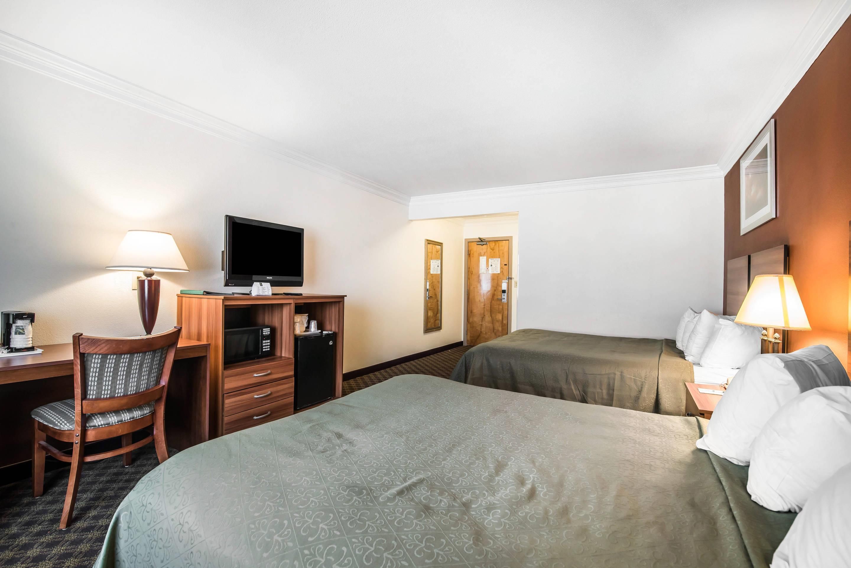 A hotel room with a desk, chair, television, two beds, and a small refrigerator.