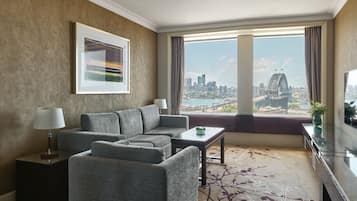 A modern hotel room with a sofa, a small table, a lamp, and a large window offering a city view.