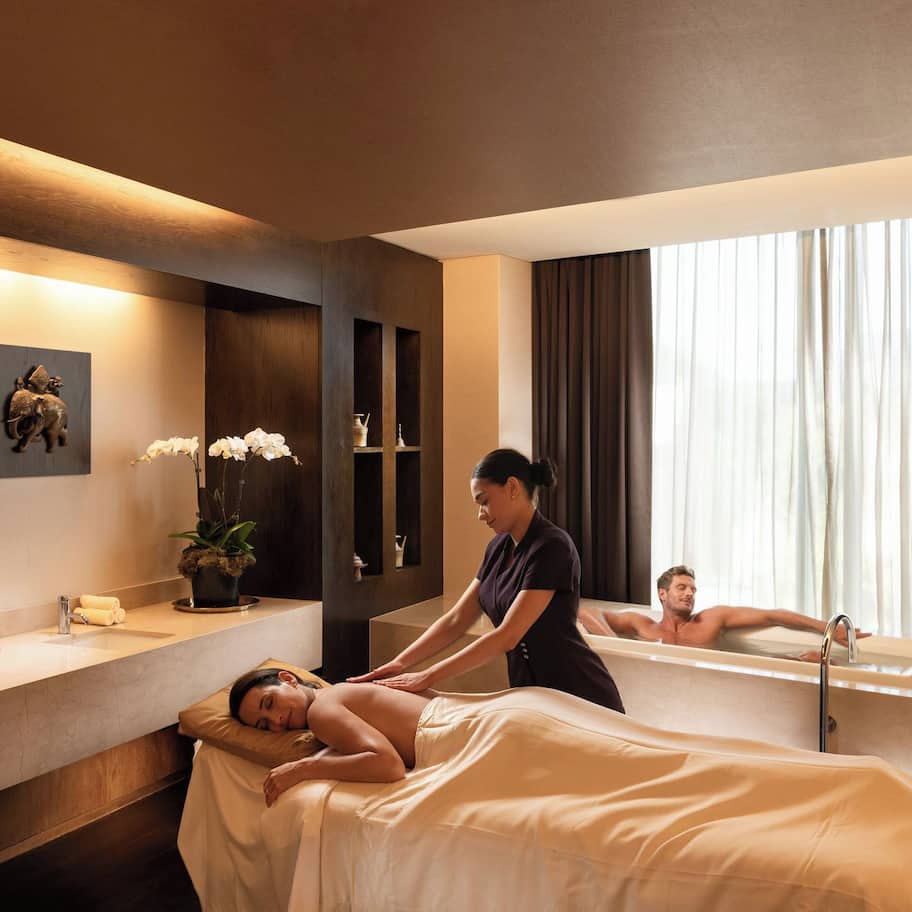 A spa room with a massage table, a bathtub, and a large mirror.