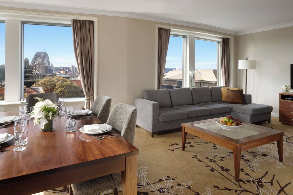 A modern living room with a dining area, grey sofa, wooden coffee table, and large windows with a city view.