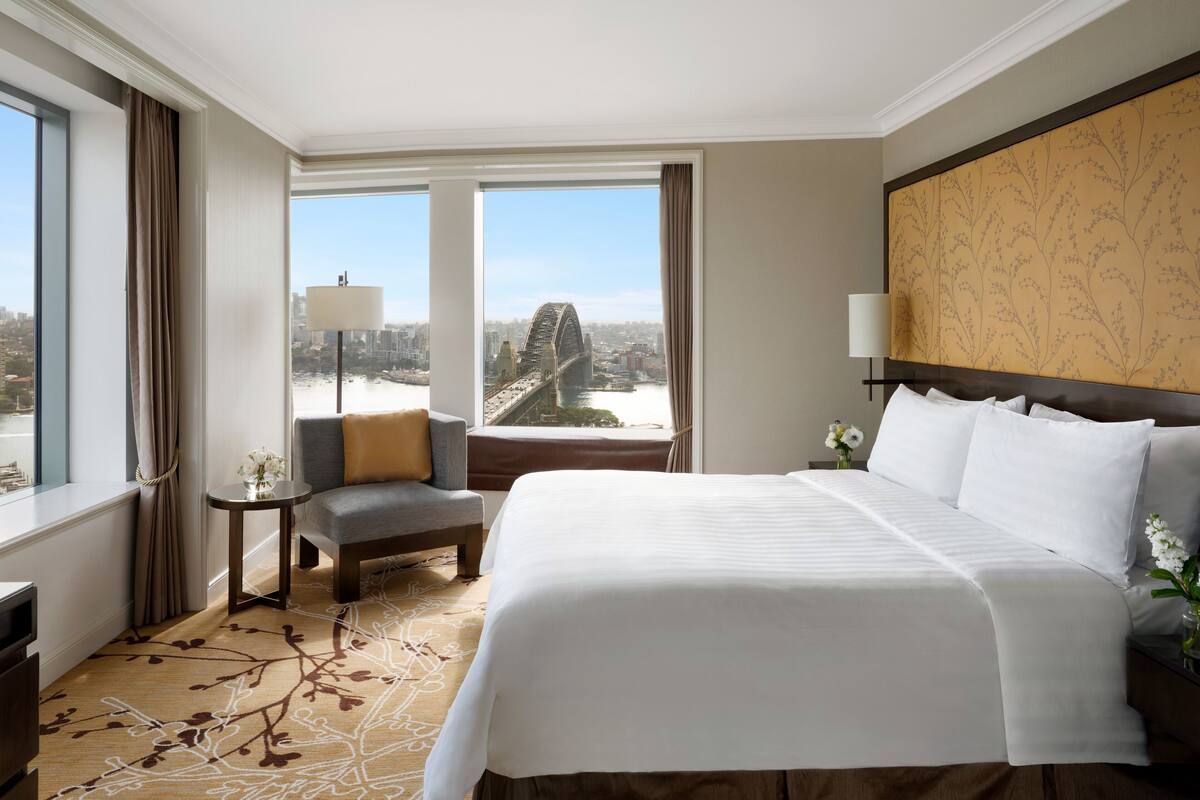 Ein Hotelzimmer mit einem großen Bett, einem Sessel, einem kleinen Tisch und Blick auf eine Brücke.