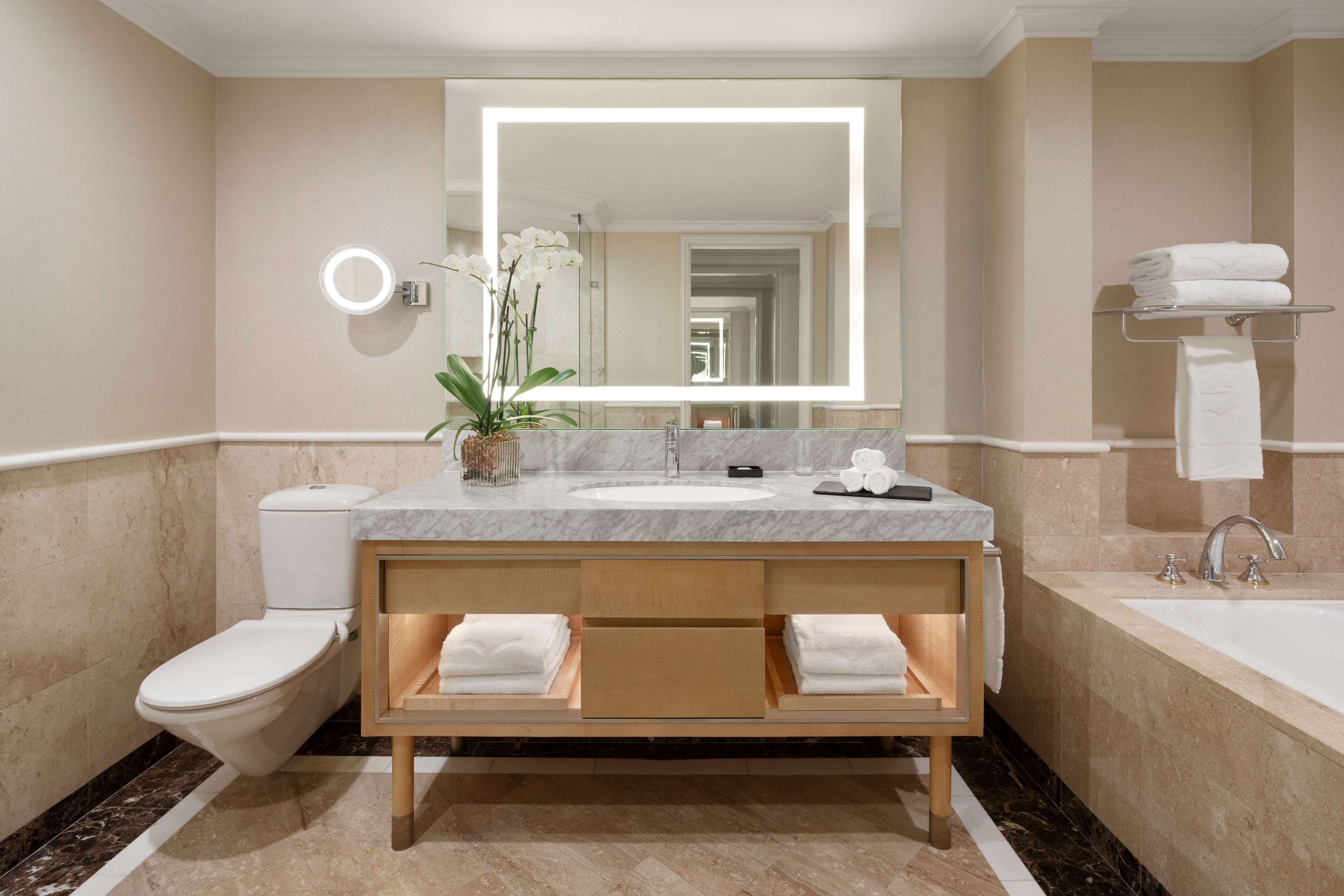 A modern bathroom with a marble sink, a large mirror, a toilet, and a bathtub.