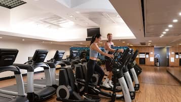 Un gimnasio con cintas de correr, bicicletas estáticas y un espejo grande.