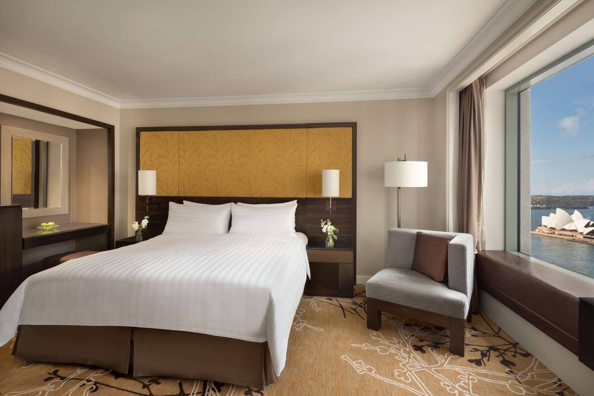 A hotel room with a large bed, a chair, a nightstand, a lamp, and a view of a body of water.
