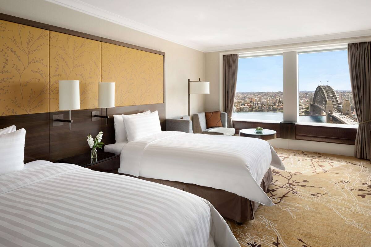 A hotel room with two beds, a sofa, a small table, and a view of a bridge.