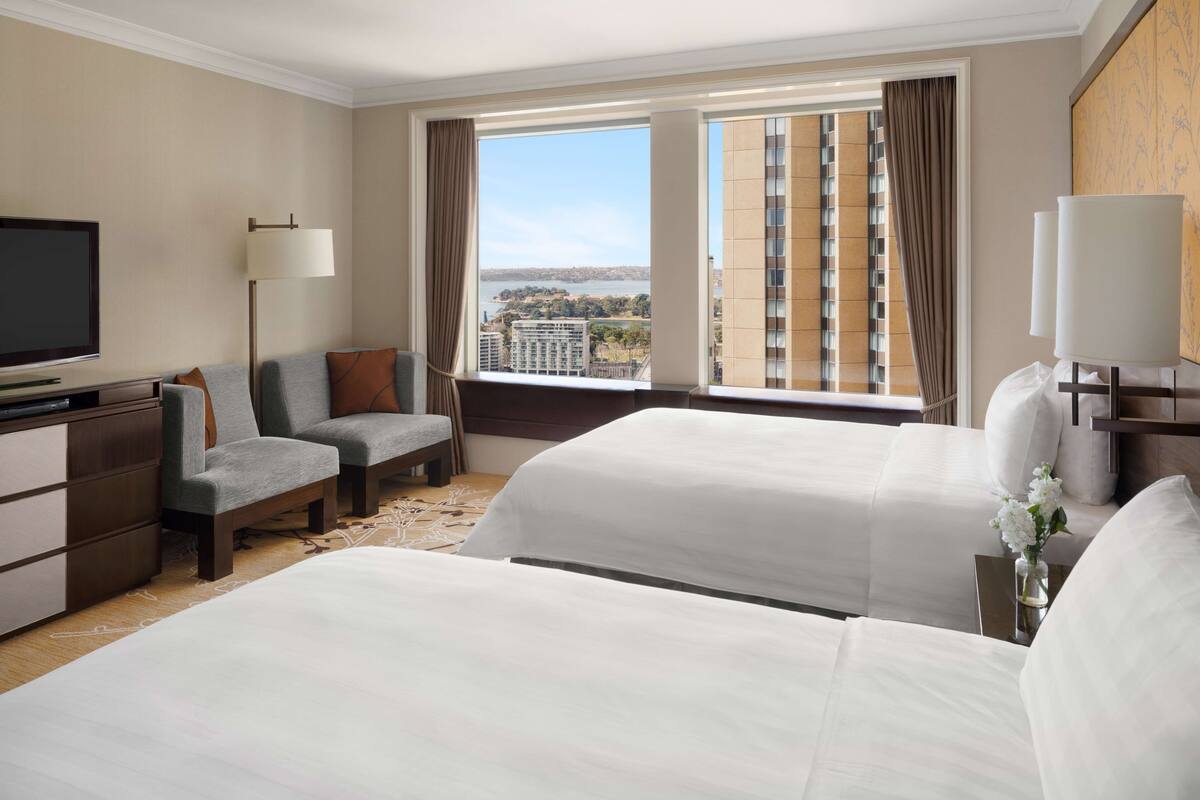 Ein Hotelzimmer mit zwei Betten, einem Sofa, einem Fernseher und einem gro ßen Fenster mit Blick auf die Stadt.