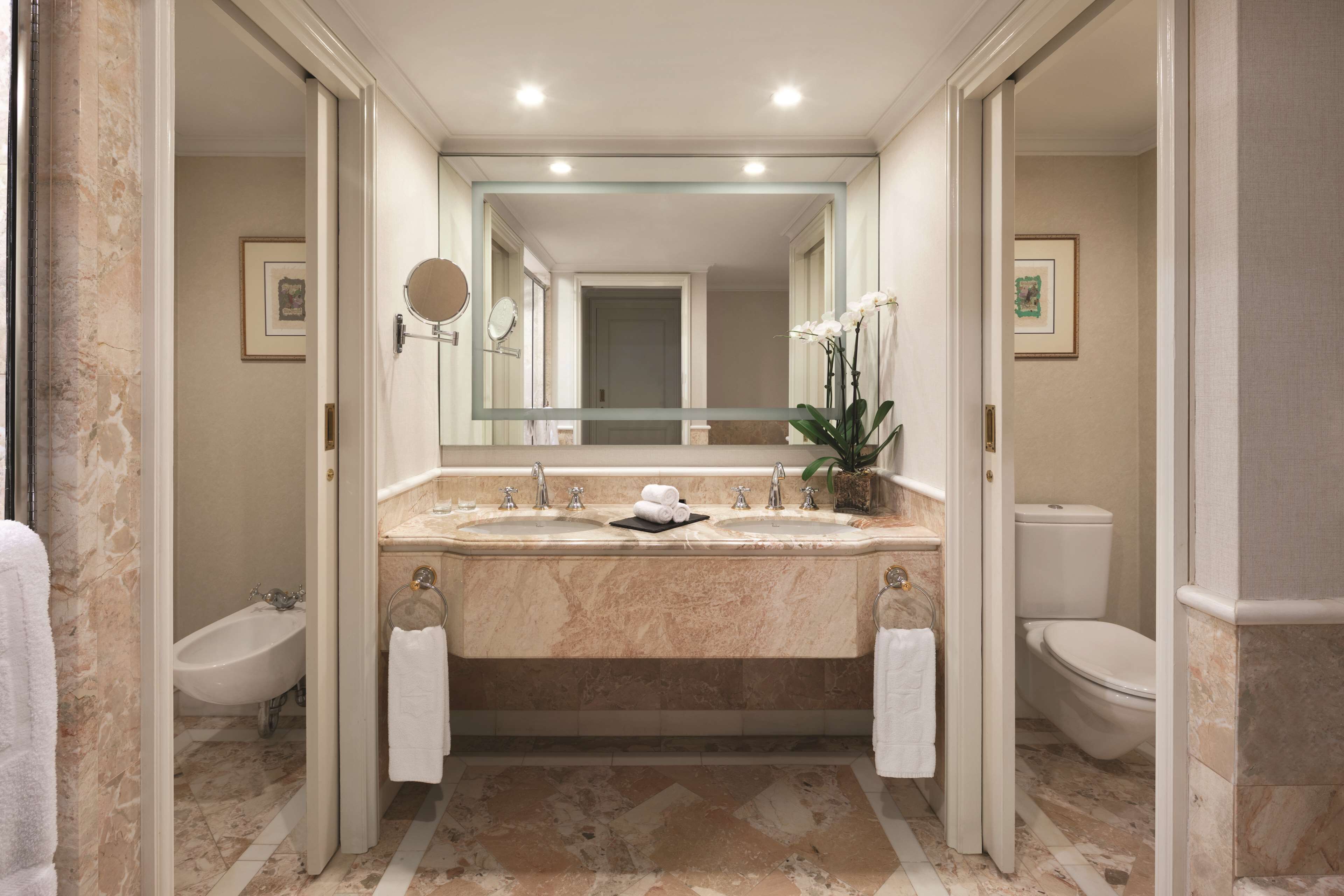 A bathroom with a marble sink, two toilets, a bidet, and a large mirror.