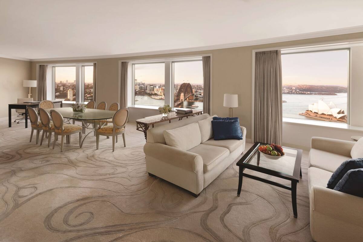 A spacious hotel room with a dining area, a sofa, and a view of a bridge and cityscape.