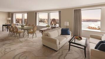 Quarto de hotel espaçoso com área de refeições, sofá e vista para uma ponte e horizonte urbano.