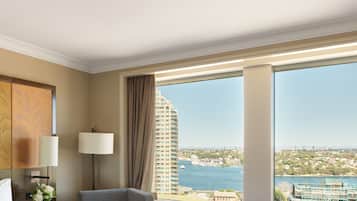 A hotel room with a large window, a bed, a chair, a small table, and a lamp.