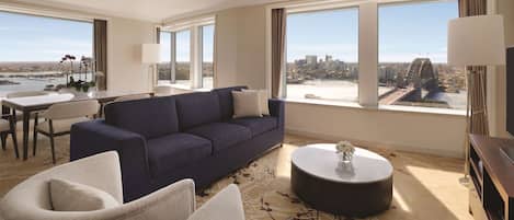 Habitación de hotel moderna con un sofá grande, una mesa de comedor y vistas a la ciudad y un puente.