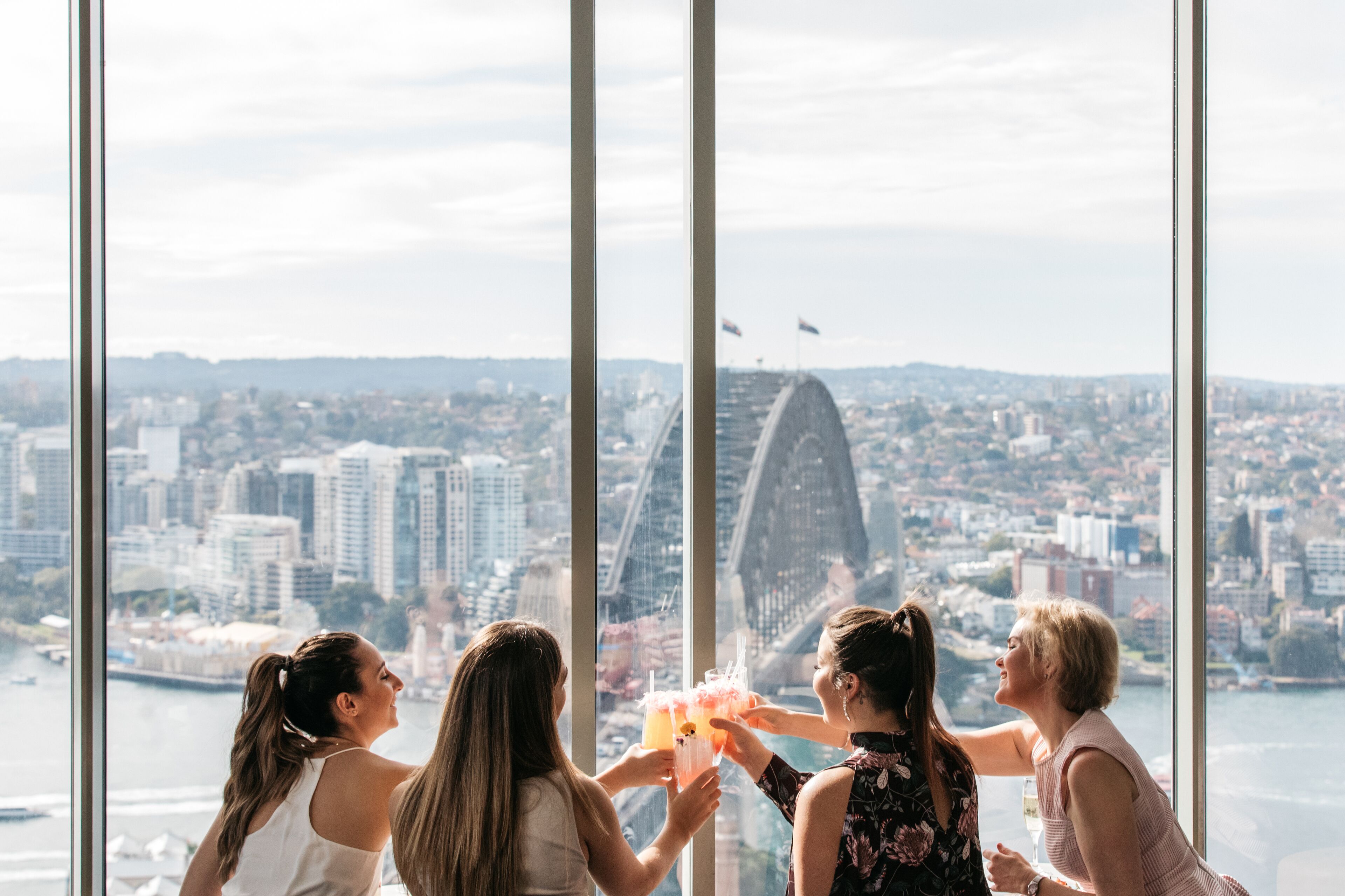 Un grupo de personas disfrutando de bebidas con vistas a la ciudad a través de amplios ventanales.