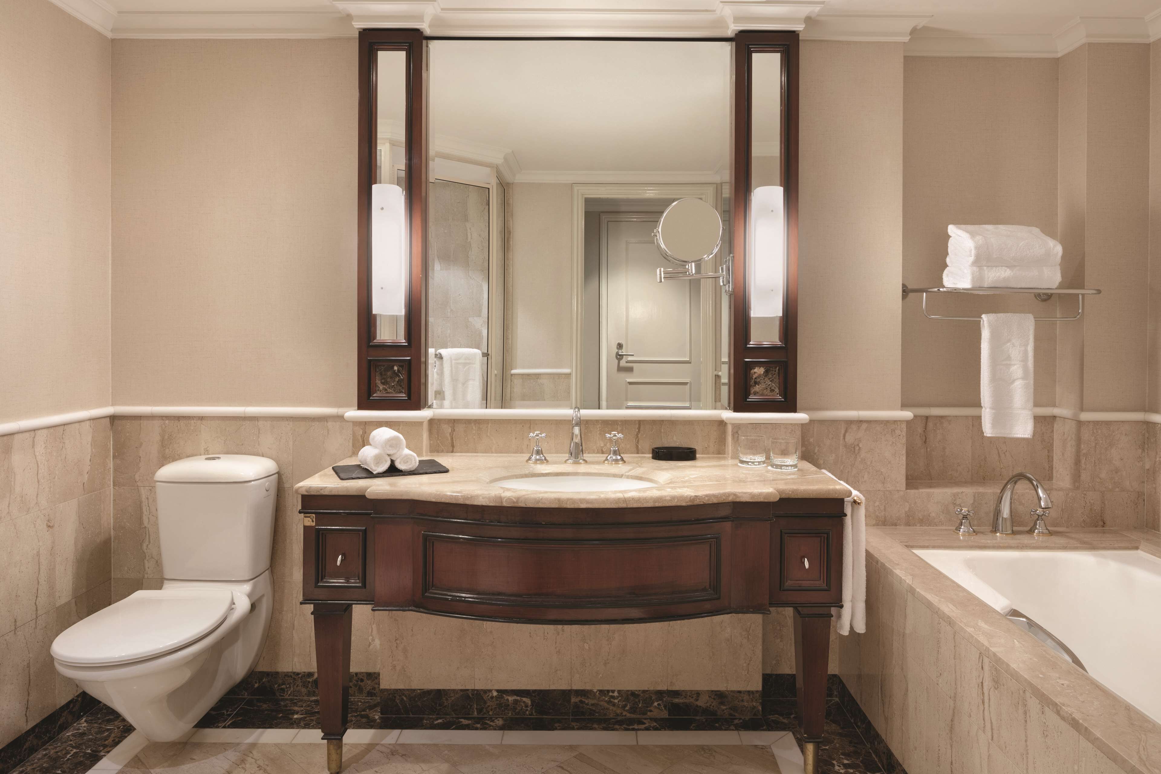 A bathroom with a marble sink, a toilet, a bathtub, and a large mirror.
