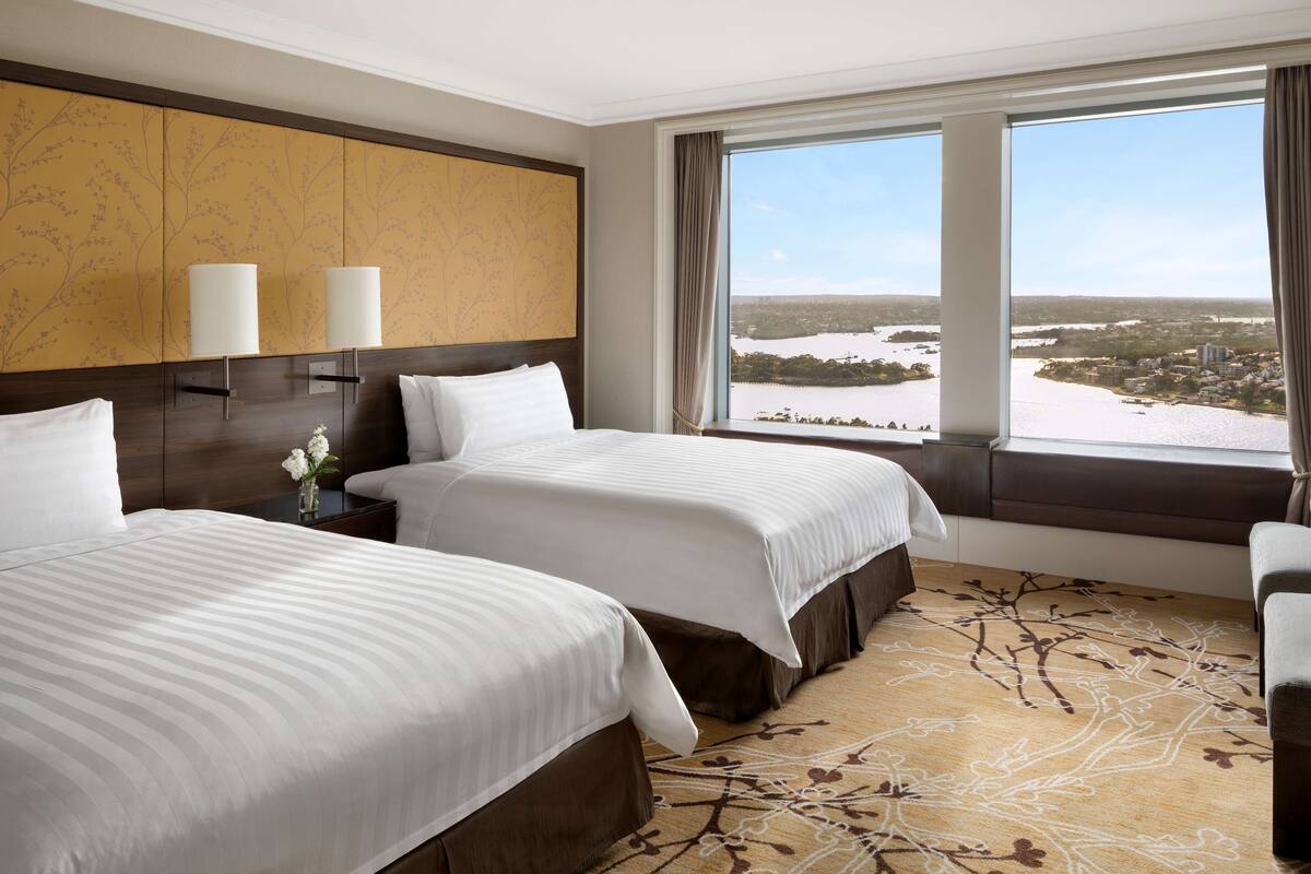 A hotel room with two beds, a large window with a view of a cityscape, and a decorative wall panel.