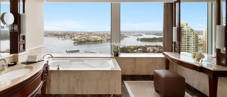 A modern bathroom with a large bathtub, two sinks, and a view of a cityscape and water body.