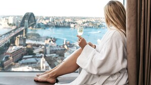 A person sitting by a window with a city view, holding a glass of wine. - Shangri-La Sydney (The Rocks)